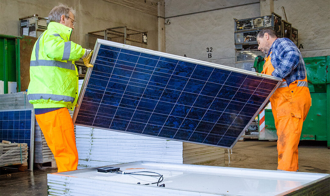 Foto: Zwei Mitarbeiter, die ein Photovoltaikmodul hochheben